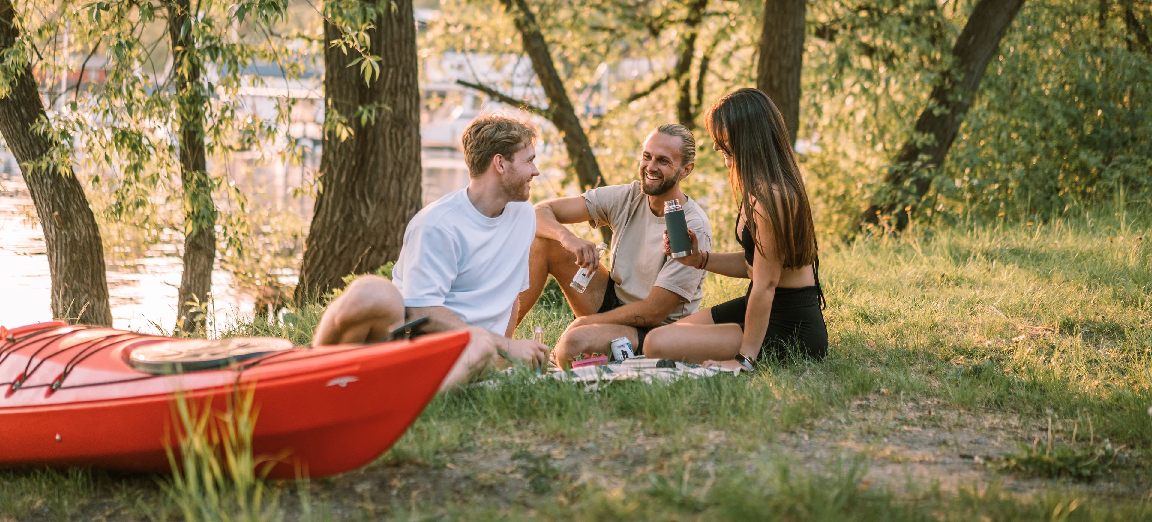 Group of friends having a picnic next to the shore on a sunny evening after paddling kayaks together. Kayaks next to them.