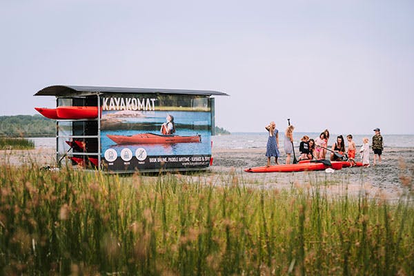 A KAYAKOMAT automatic kayak rental station on a beach. A KAYAKOMAT operator shows a group of families how to put their kayaks into the water.