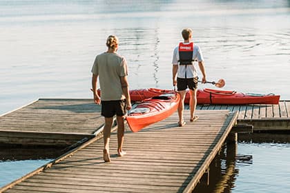 Two friends bring their KAYAYKOMAT kayaks from the rental station to the dock.